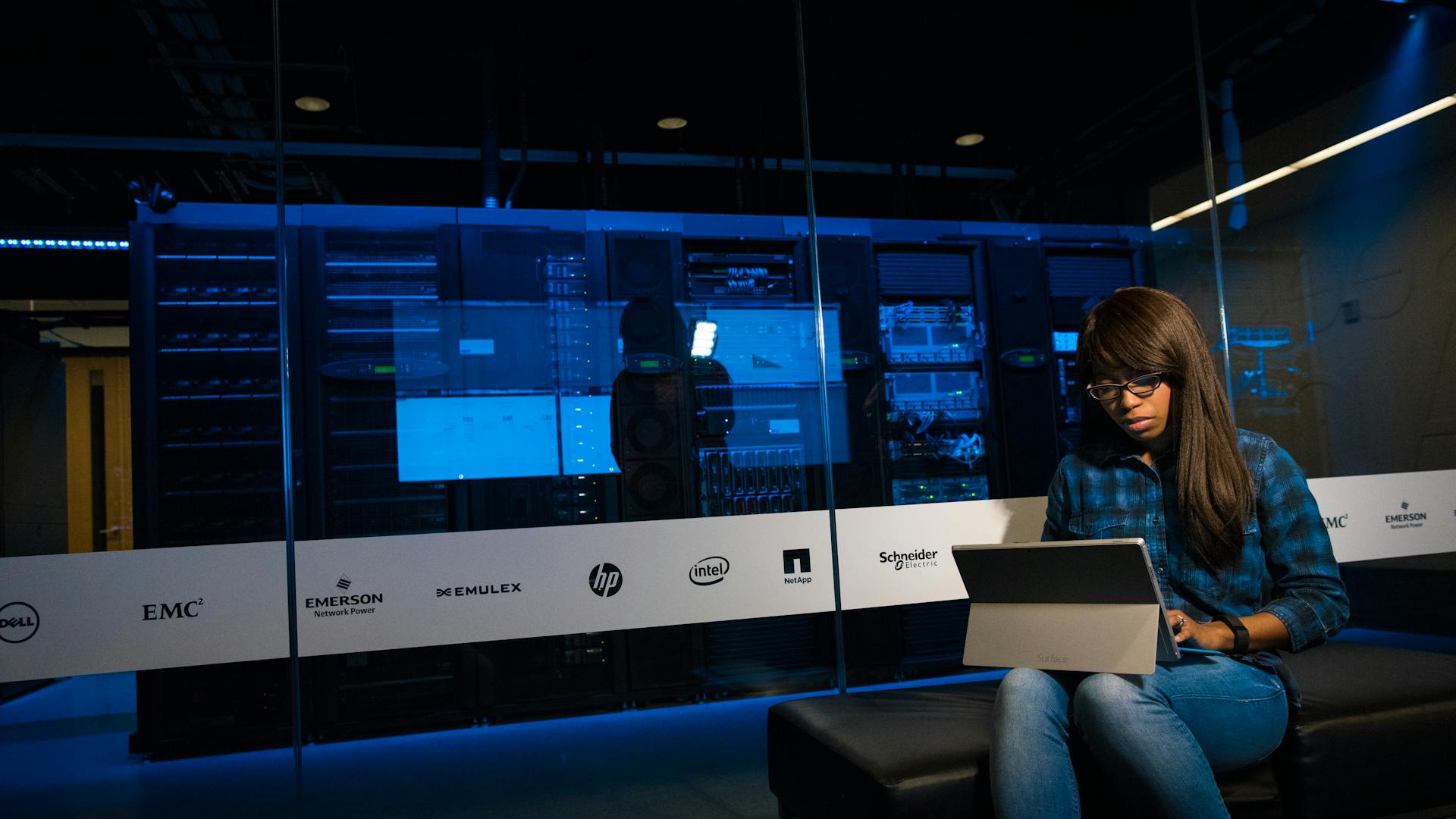Woman using a laptop in a server room, showcasing modern technology and work environment.