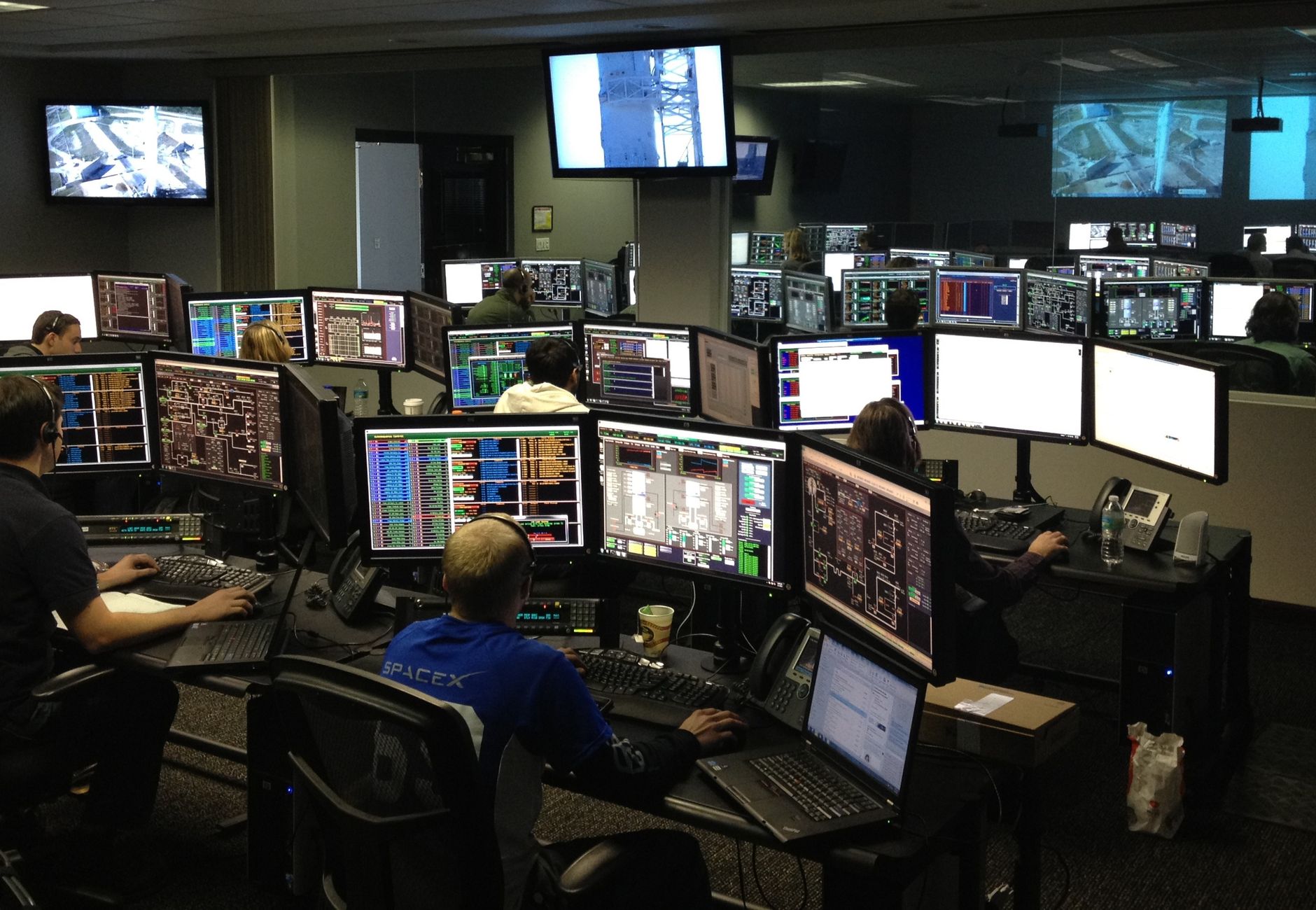 A bustling control room with people working on multiple computer monitors.