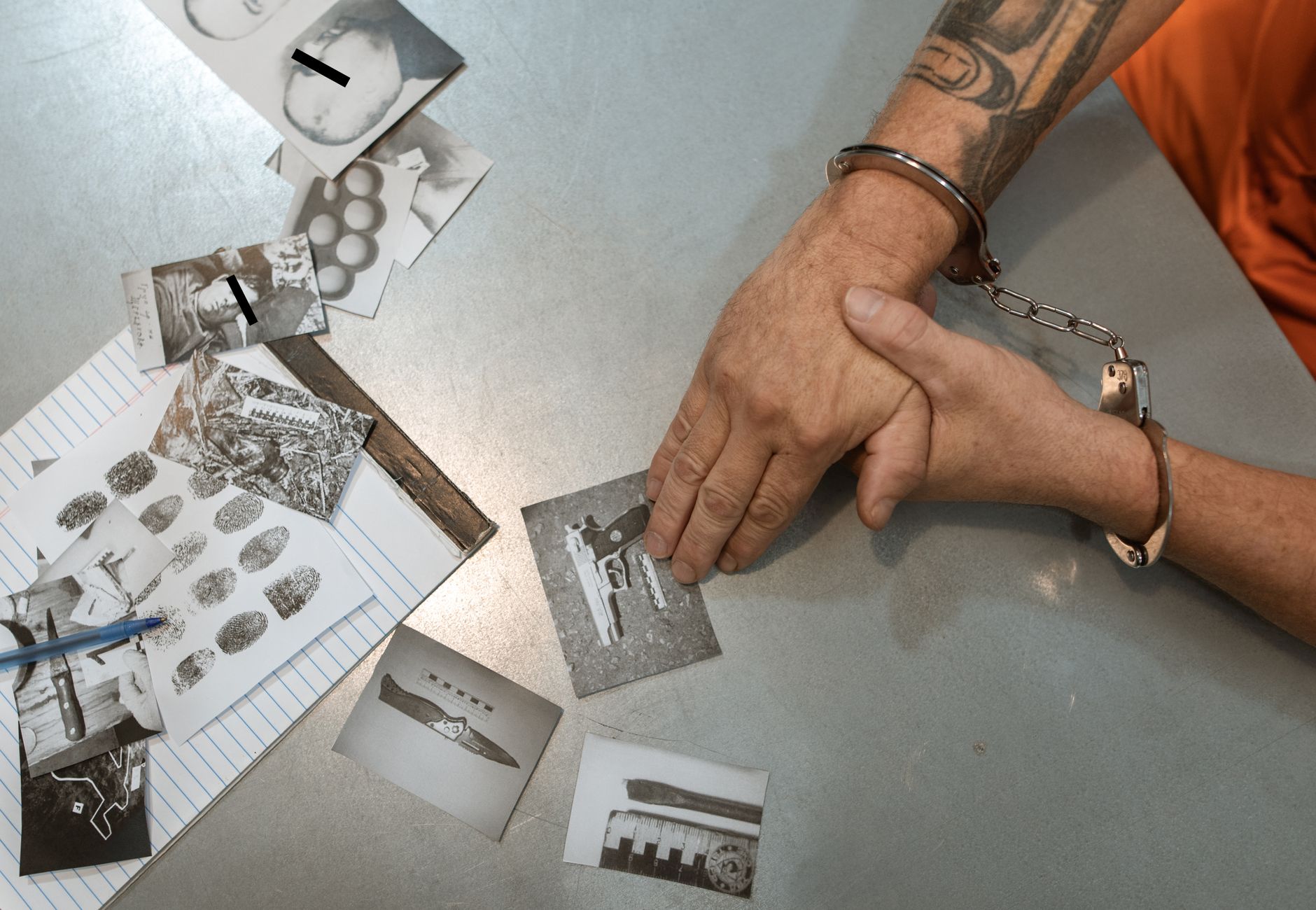A handcuffed individual examines evidence photos and documents during an investigation.