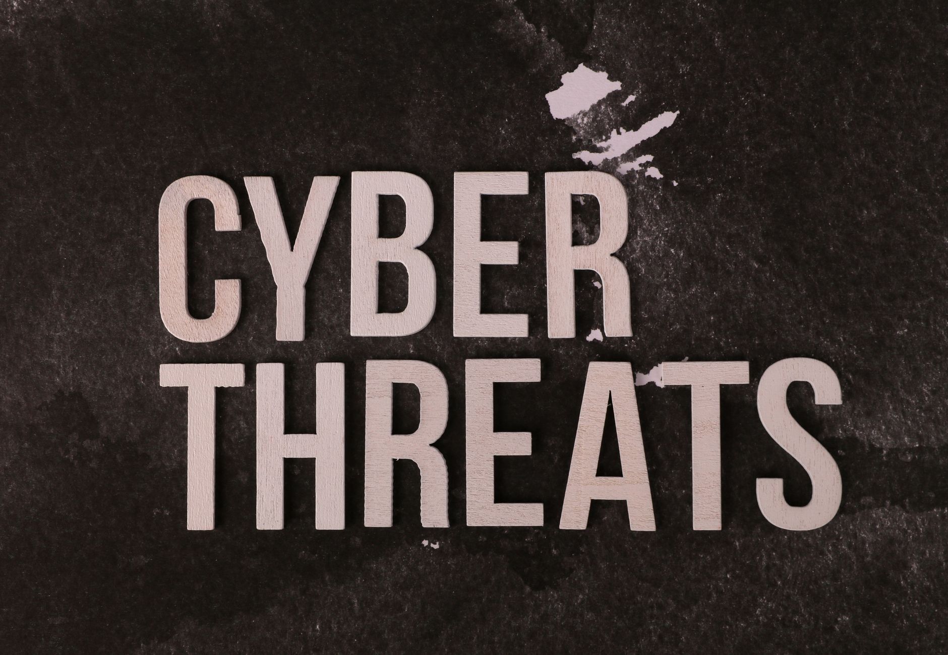 The phrase 'Cyber Threats' displayed on a textured dark background, emphasizing digital security.