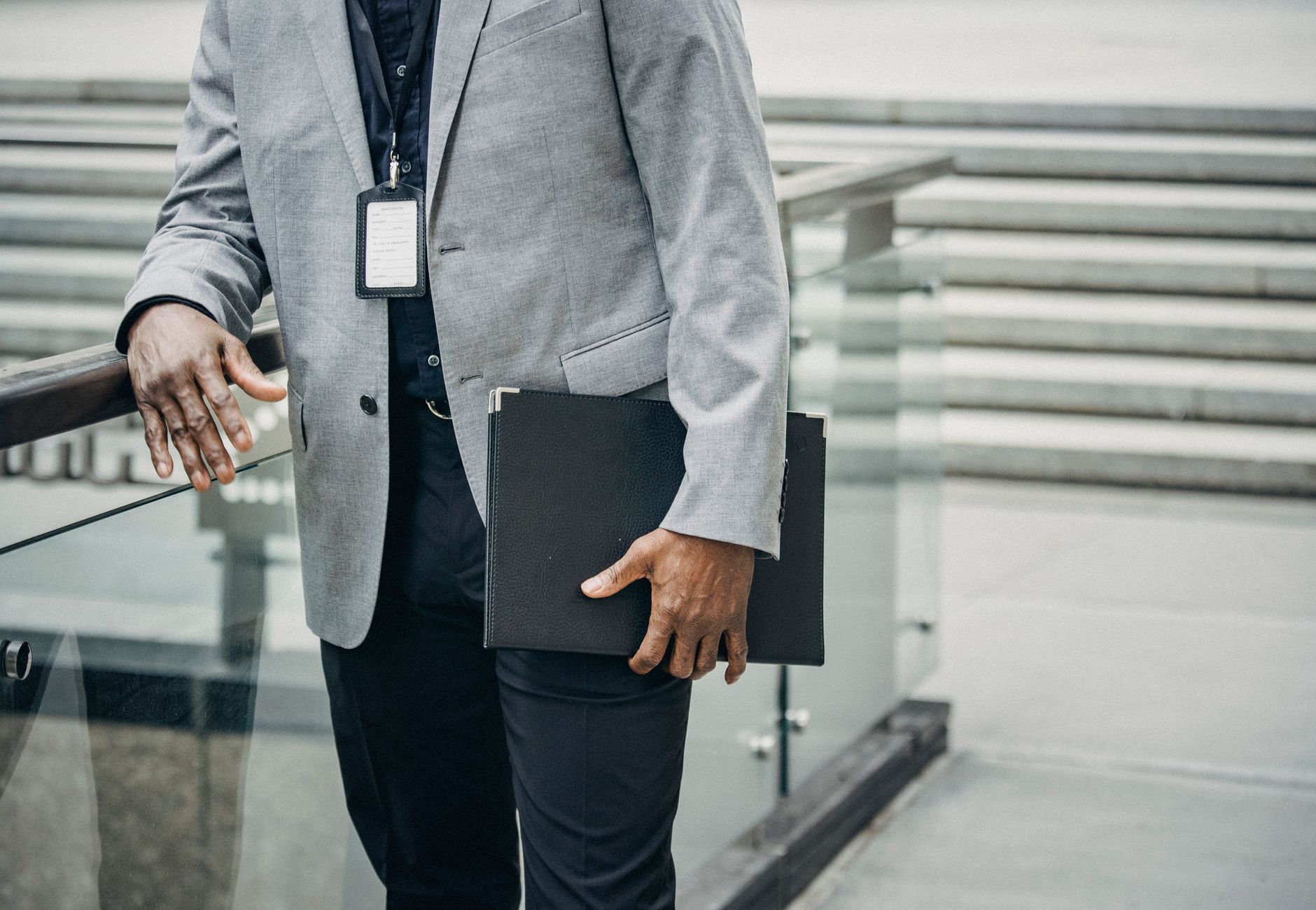 Crop unrecognizable African American entrepreneur leaning on fence and carrying folder with papers in soft daylight
