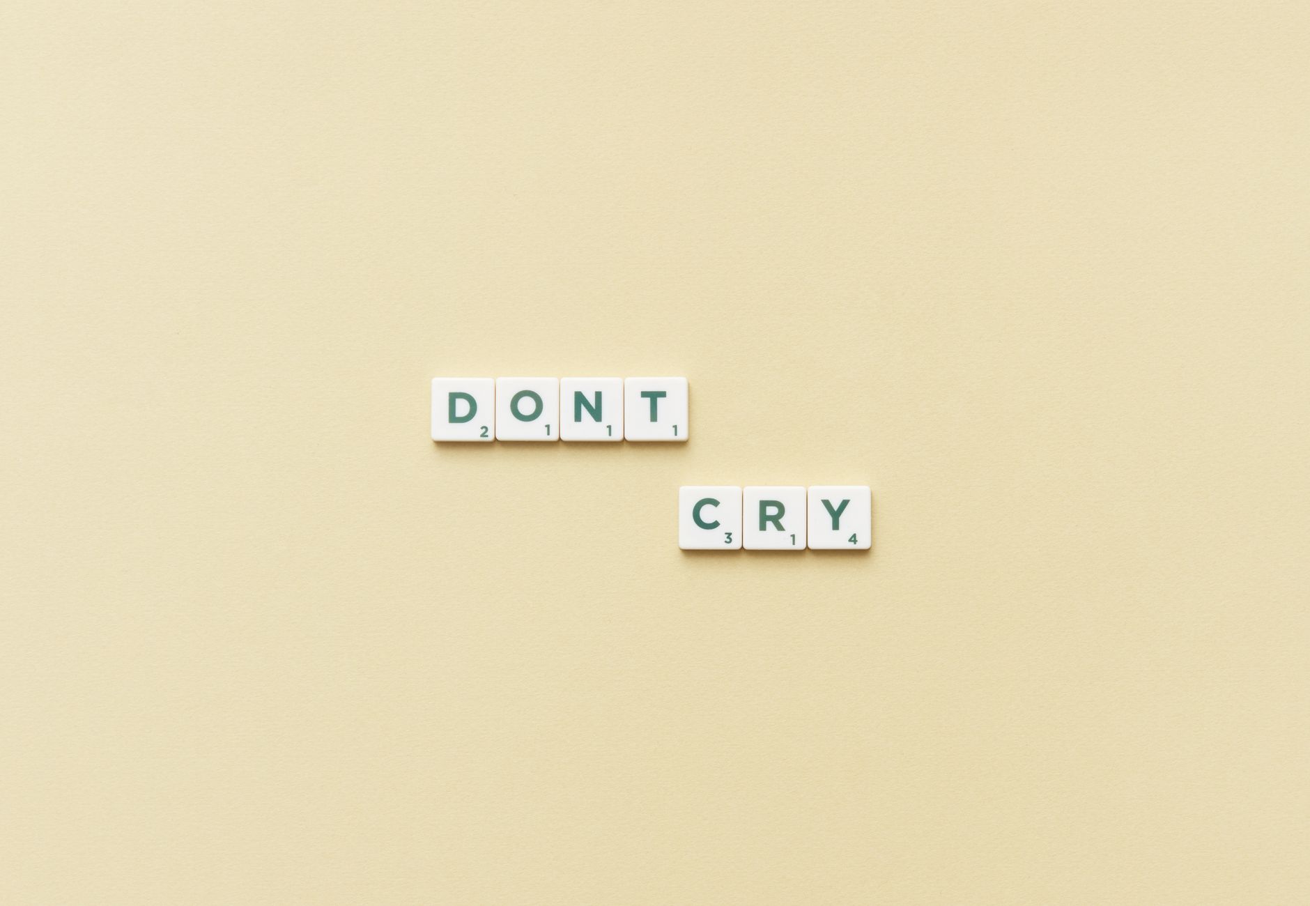 Scrabble tiles forming the phrase 'Don't Cry' on a simple yellow background, top view.