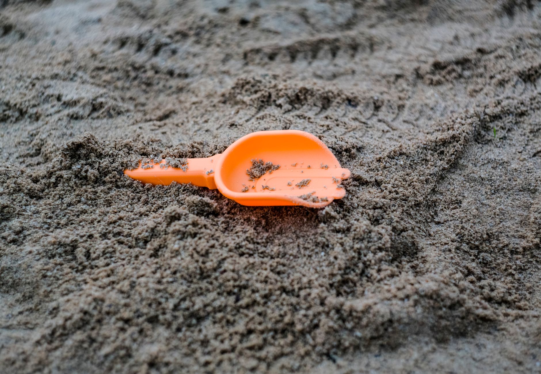 From above of plastic orange sandbox play shovel for children lying on sandy ground