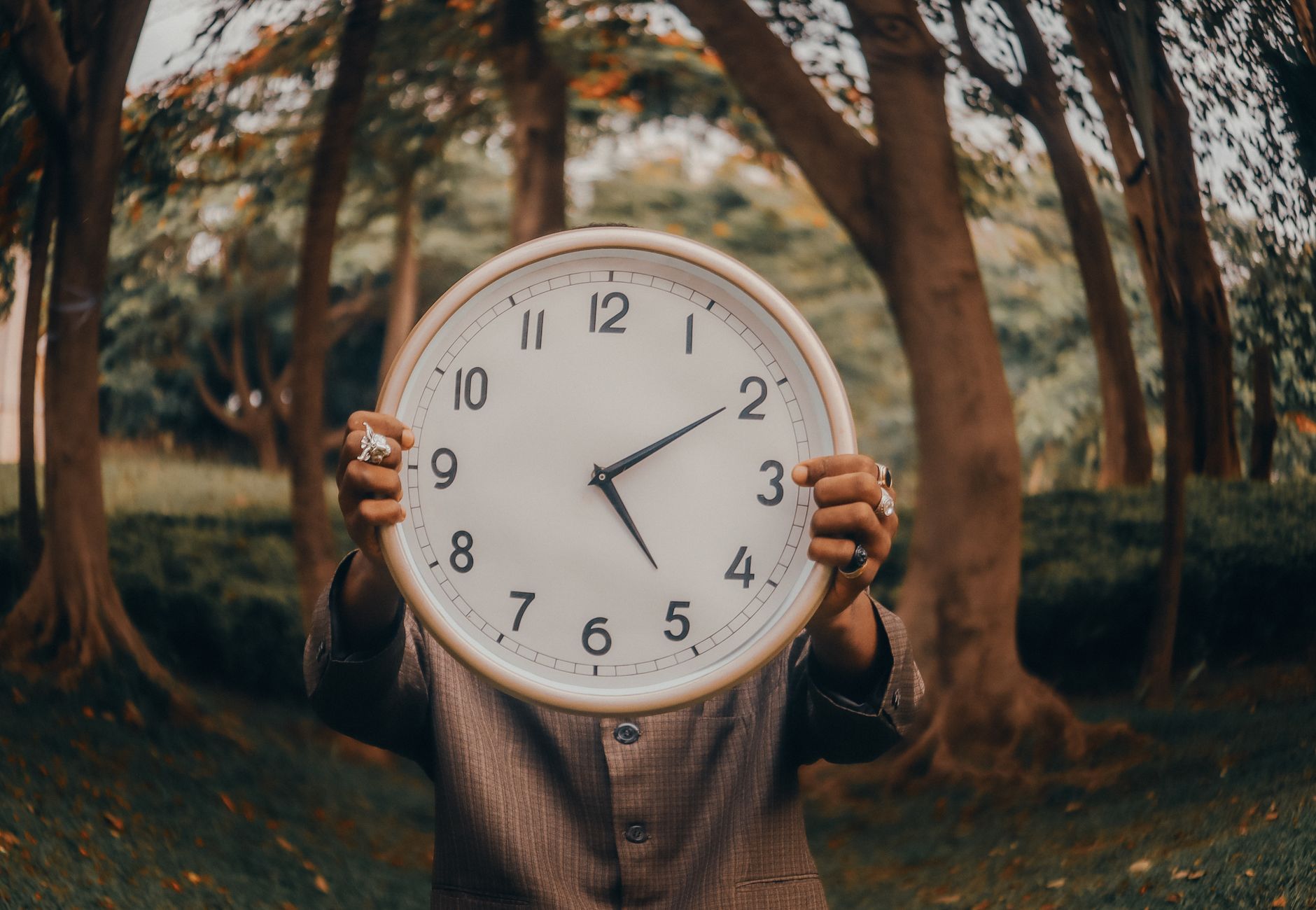An individual holding a large clock in an outdoor forest environment, symbolizing time.