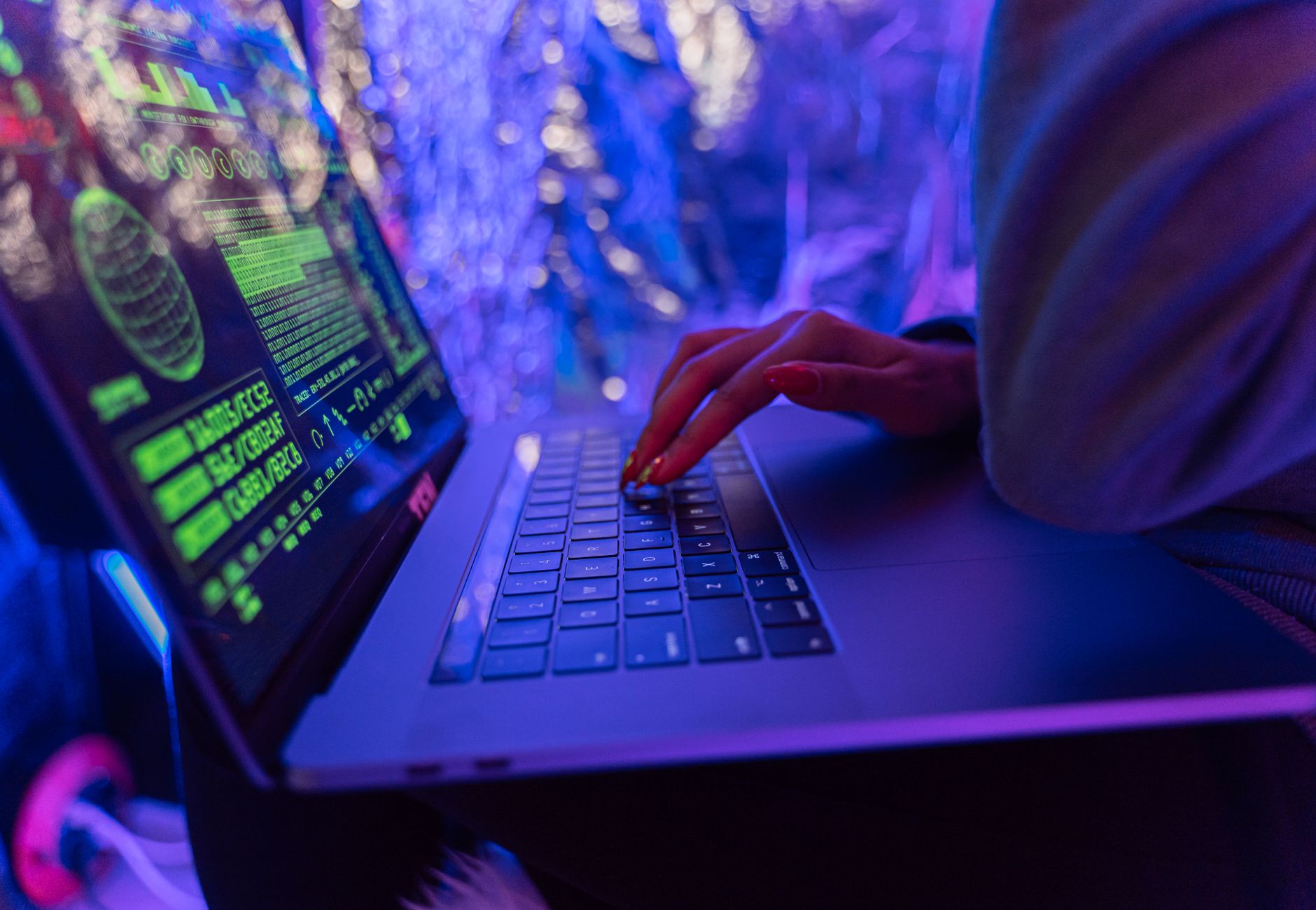 Close-up of hands typing on a laptop displaying cybersecurity graphics, illuminated by purple light.